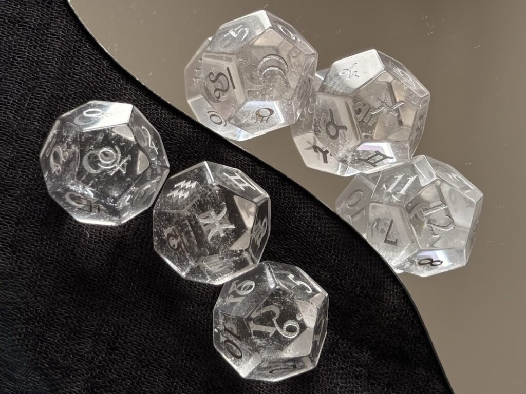 A set of clear crystal 12-sided astrology dice on a black and white reflective background, perfect for a beginner's first astrology dice use